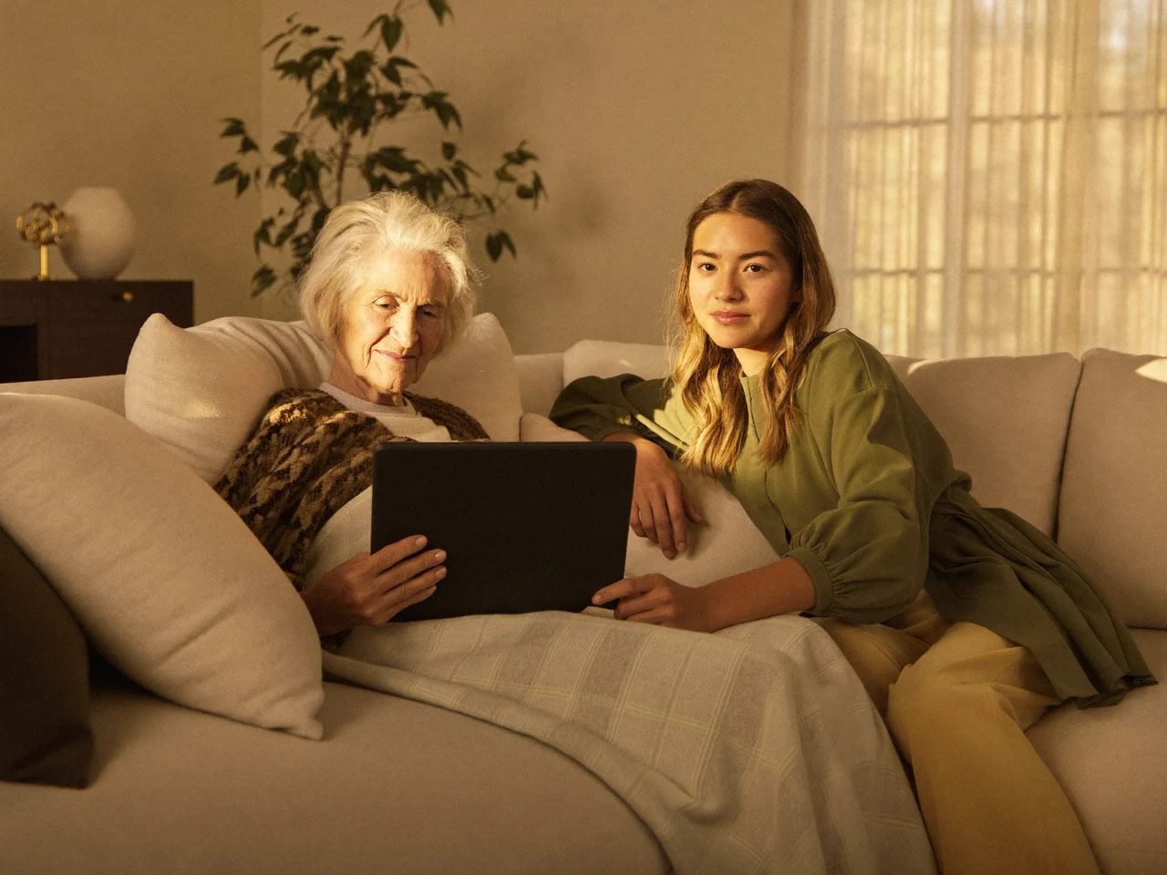 Illustrazione: una signora e un'aiutante sul divano guardano insieme un tablet, sorridendo.